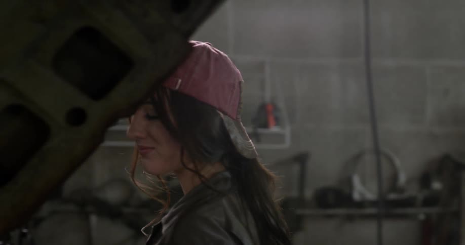A woman in a red hat walks behind a car