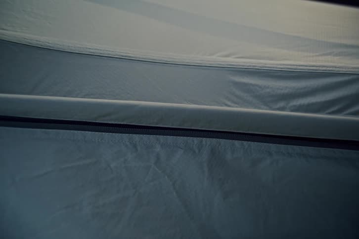 A close-up shot of a hand zipping up the flap of a camping tent in the dim light