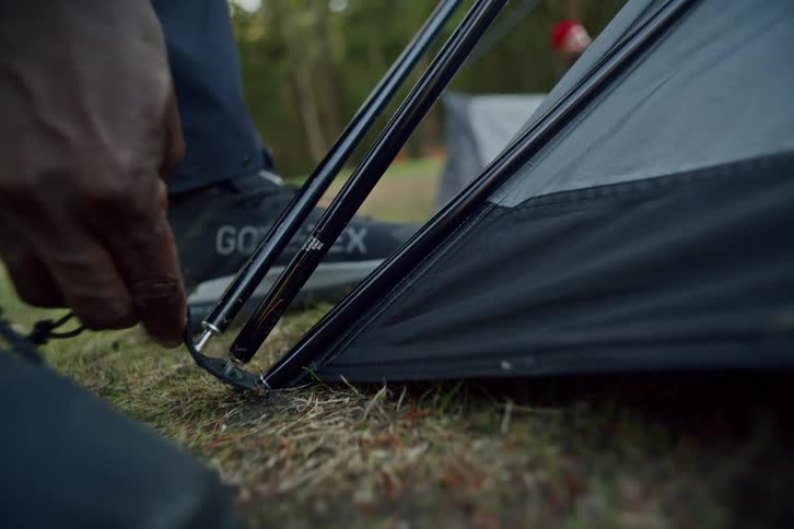 A close-up shot of a person's hand inserting a pole into the corner of a tent while setting up camp