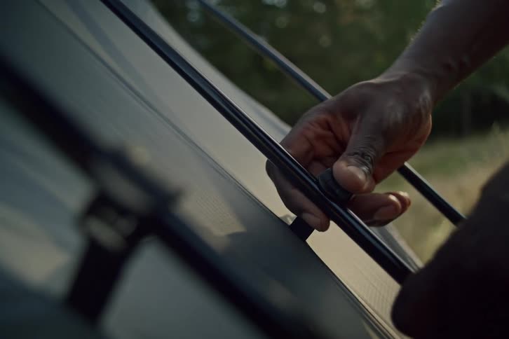 Close-up shot of a man's hands clipping the fabric of a tent to the poles while setting up camp outdoors