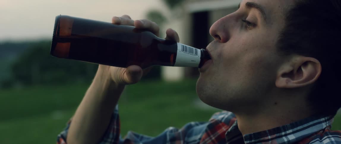 A man laughs and takes a drink of beer