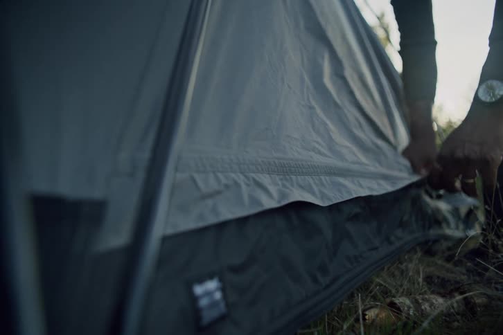 A slow motion close-up of a man zipping up his tent while setting up camp in the woods at sunrise