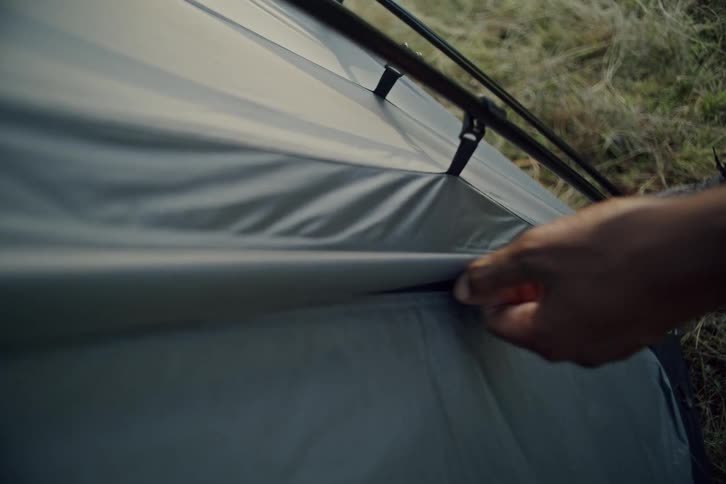 Close-up slow-motion shot of hands zipping up a modern grey camping tent outdoors