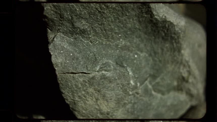 A vintage macro shot pans across the textured surface of a jagged rock as dramatic shadows shift and change