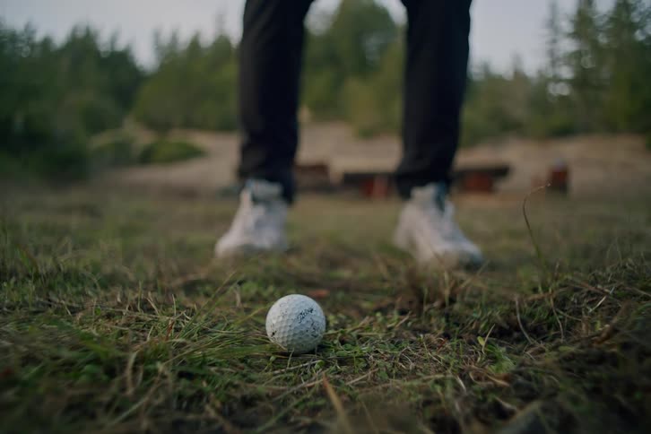 Golfer hits a golf ball out of the rough grass in a dramatic slow-motion close-up