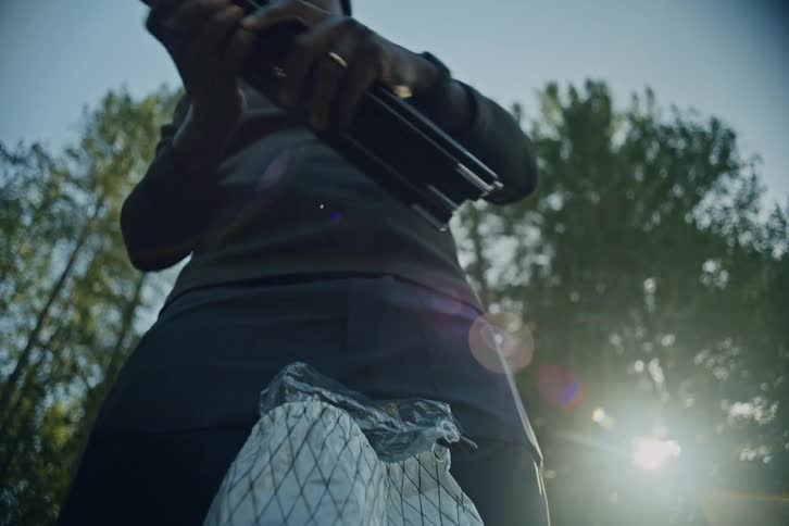 Cinematic low-angle view of a man unpacking his gear and assembling tent poles as he prepares to camp in the woods at sunrise