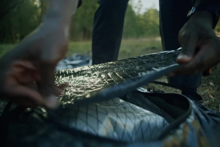Slow motion close-up of a camper's hands unpacking gear from a large duffel bag in the woods