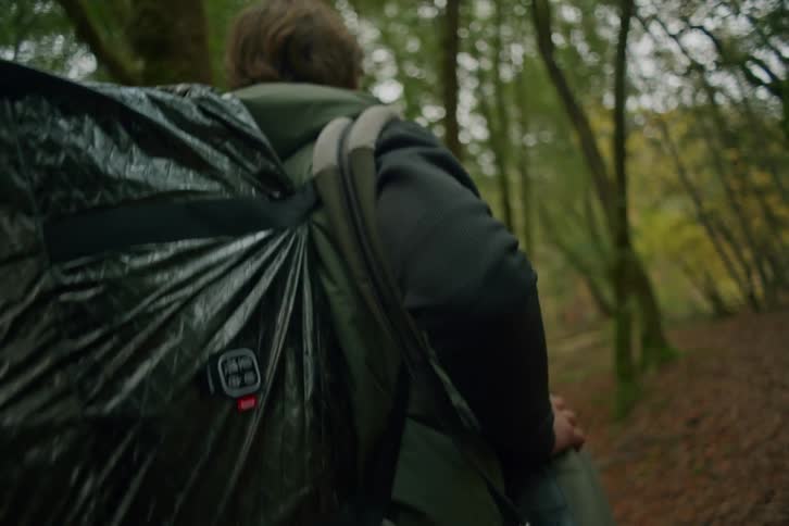 A person with a large backpack hikes along a trail through a lush green forest