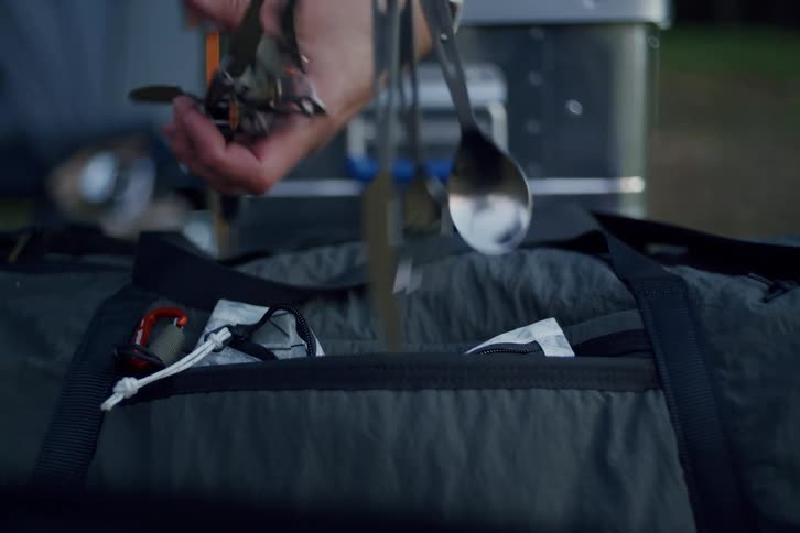 Slow motion close-up of a person unpacking a set of camping utensils from a duffel bag