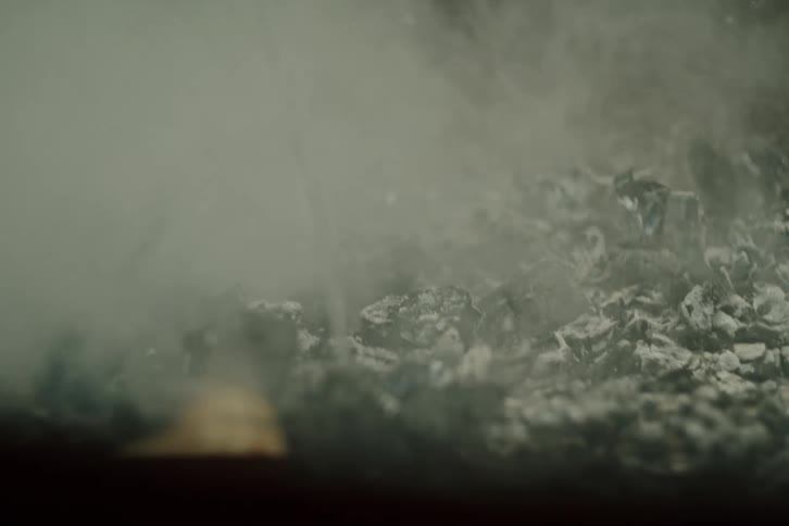 Slow motion close-up of water extinguishing smoldering charcoal embers, kicking up ash and steam