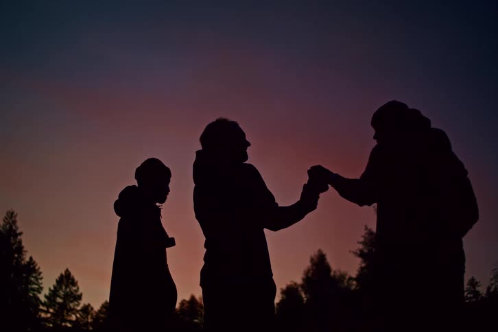 Silhouettes of three friends sharing a drink and enjoying the beautiful twilight colors in the sky
