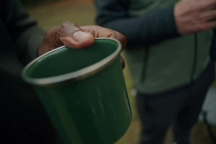 Close-up of a person holding a green enamel camping mug outdoors