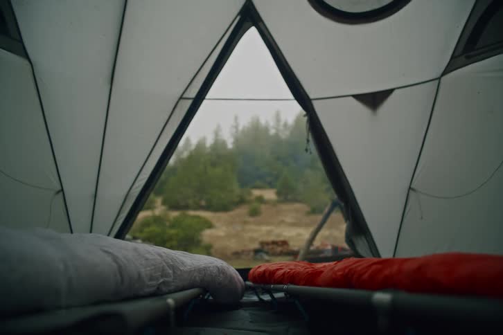 A cozy view from inside a tent looking out at a smoking campfire in a foggy forest clearing