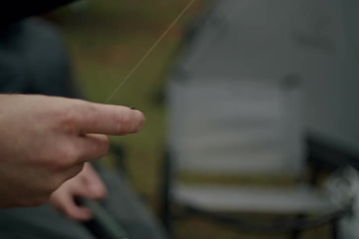 A close-up shot of a man's hands tying a knot for a small fly fishing lure onto his line