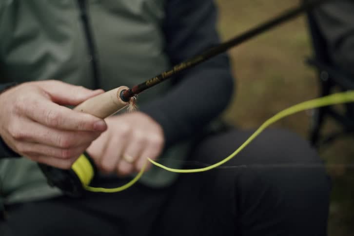 A fly fisherman carefully threads the line through his fishing pole before casting