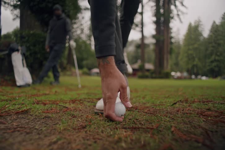 A low angle close up of a golfer placing a tee and ball into the ground before taking a practice swing