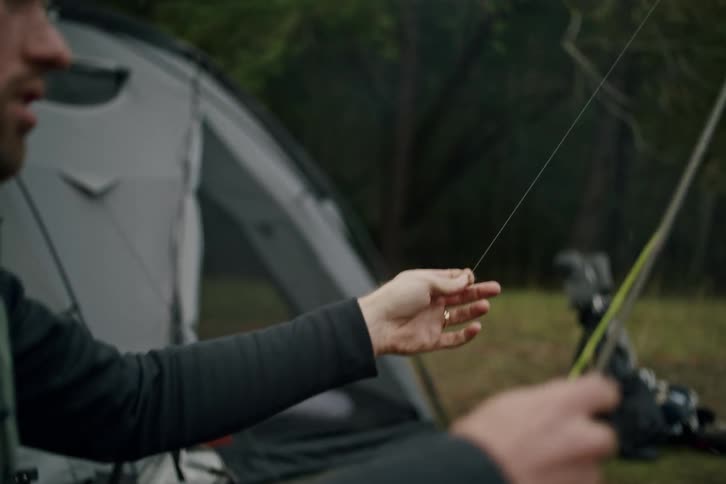Focused fisherman practices his fly casting technique in slow motion with a tent in the background