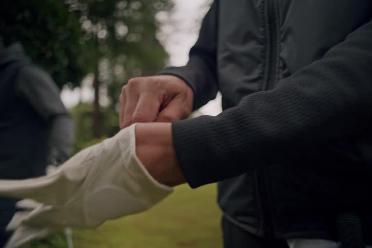 A man carefully puts on his white golf glove while standing on a lush green course