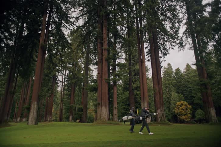 Two men carry their clubs while walking across a beautiful golf course nestled within a forest of giant redwood trees
