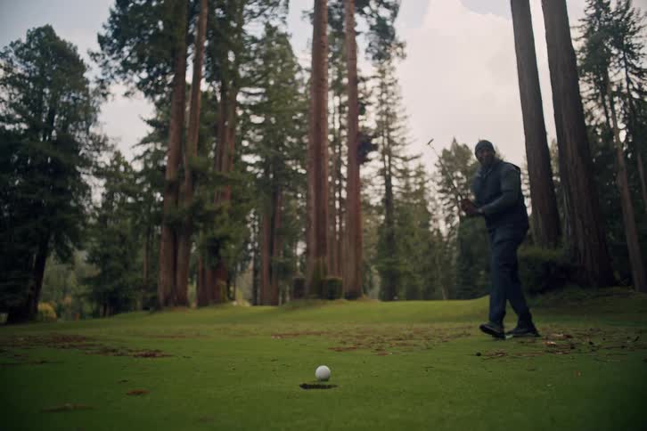 A golfer celebrates making a successful putt on a scenic course nestled among towering redwood trees