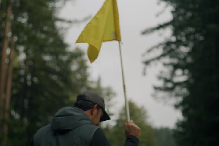 A male golfer removes a yellow flag from a golf course hole as another player walks past
