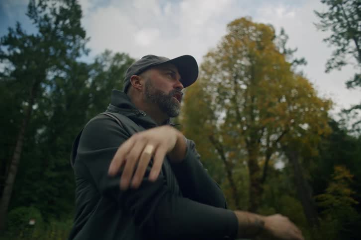 A man in a hat uses binoculars to observe nature in a tranquil forest setting during the autumn