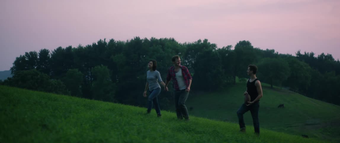 A trio of people walk up a green grassy hill