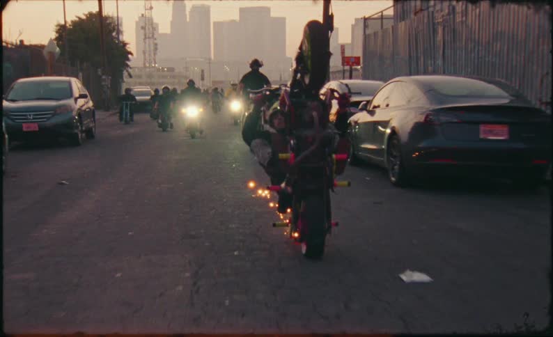 Vintage-style footage of a motorcyclist performing a wheelie with sparks while riding with his crew through the city at sunset