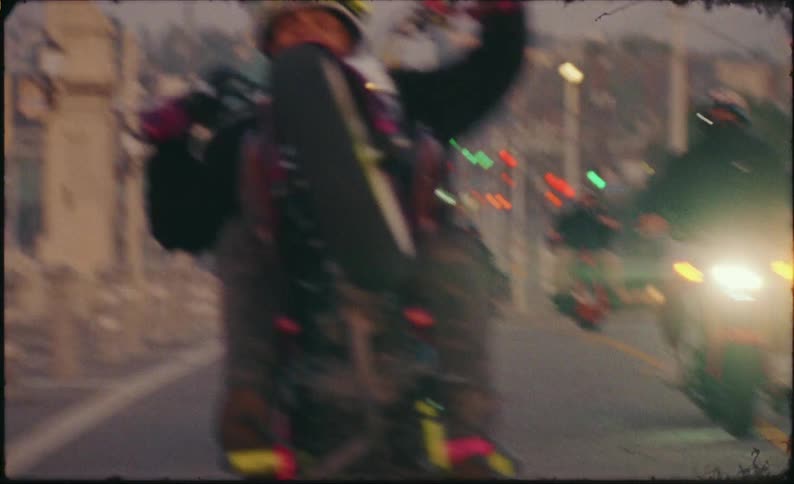 A smiling biker performs a long wheelie while leading his crew on motorcycles across a city bridge at dusk in slow motion