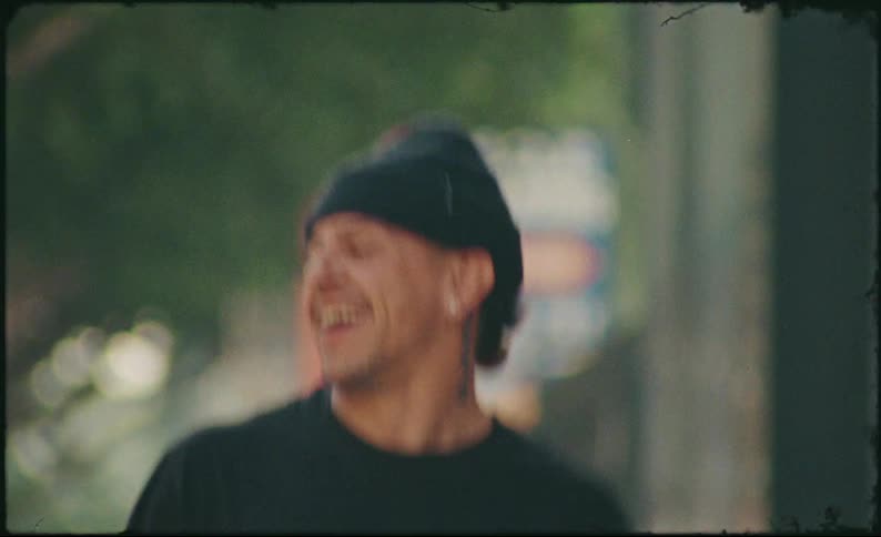 A boy and a man laugh and dance together on a city sidewalk in a vintage-style, handheld clip