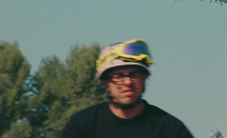A motorcycle stunt rider performs a tandem wheelie with a partner down a scenic, winding road in slow motion