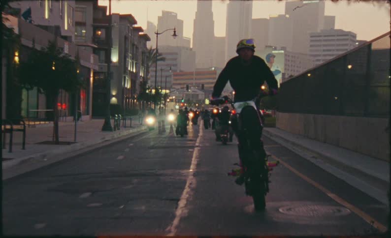 A motorcycle rider performs a long wheelie with his friends through the city streets of Los Angeles at dusk in this retro, film-style clip