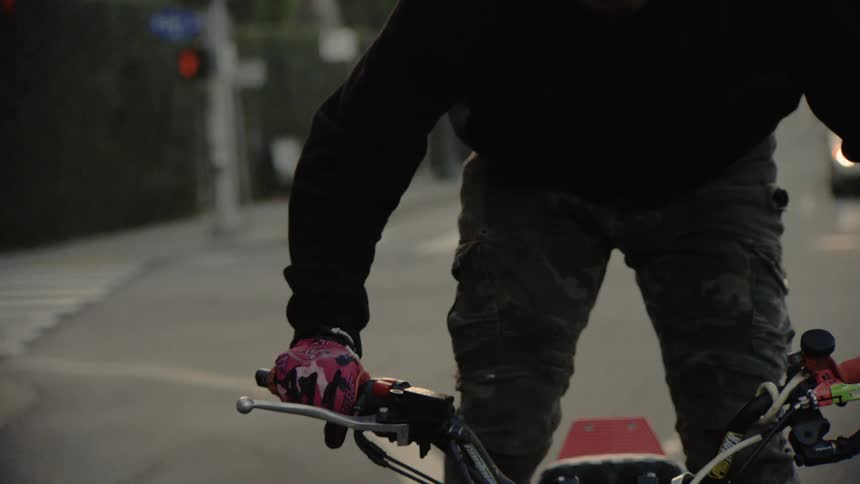 A close up slow motion shot of a motorcyclist's hands gripping the handlebars while waiting at a street intersection
