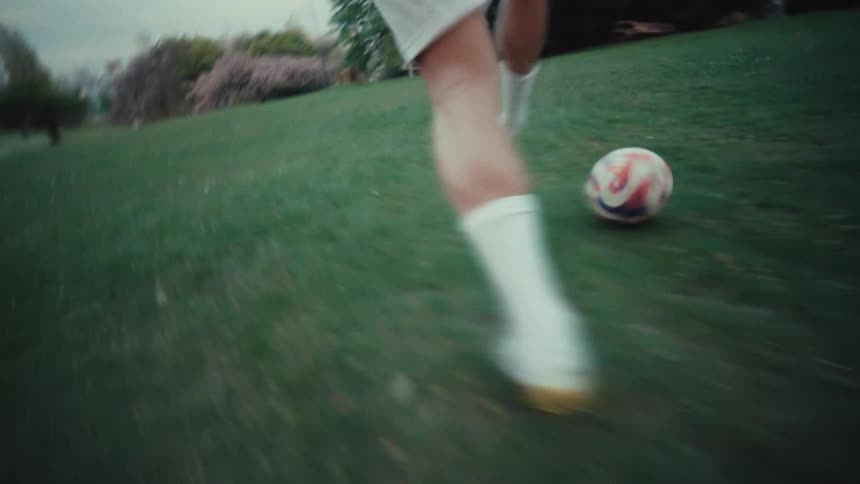 Close-up slow motion shot of a soccer player's feet in cleats running and dribbling a ball on a grassy park field at sunset