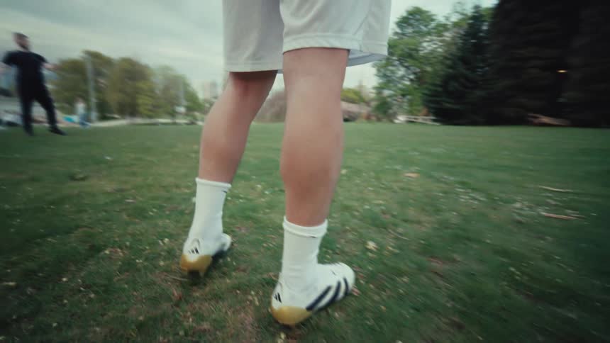 A low-angle slow-motion close-up follows a soccer player's feet as they juggle and dribble a ball in a city park