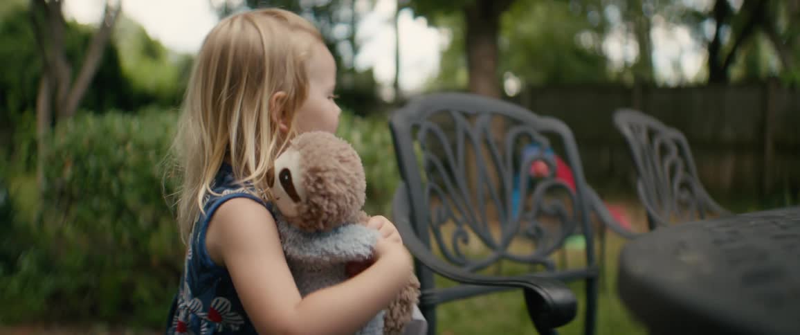 A little girl gently pets and gives a loving hug to her favorite stuffed sloth toy in the backyard