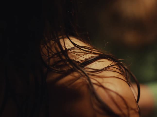 An intimate and moody close-up of wet dark hair resting on a woman's bare shoulder