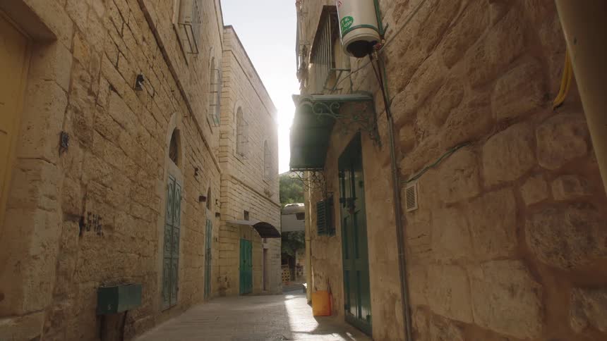 A slow push-in shot down a narrow, sunlit stone alley in an ancient Middle Eastern city