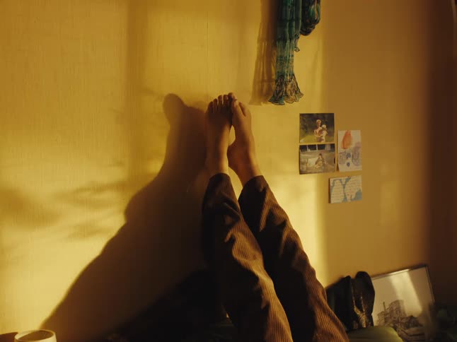 A person's bare feet are propped up against a wall, basking in the warm, golden glow of the sun in a peaceful and tranquil room