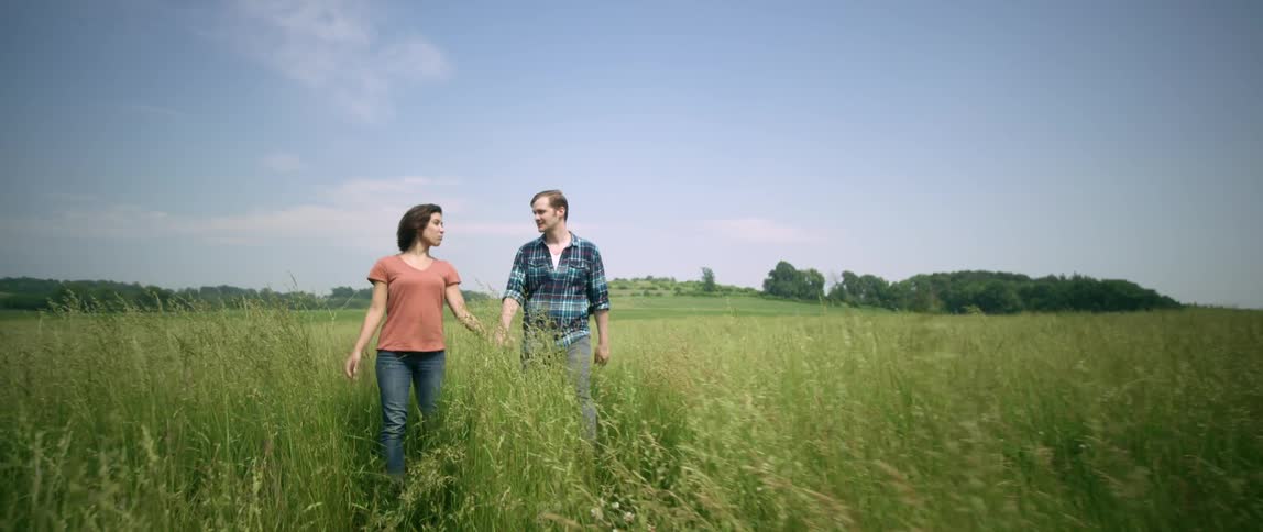 A man and woman hold hands while walking through a field