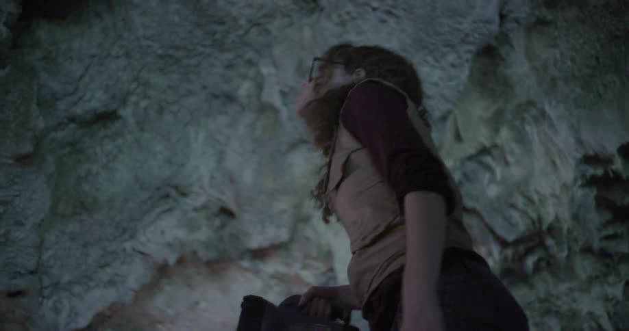 Woman shines a flashlight in a ceiling in a cave