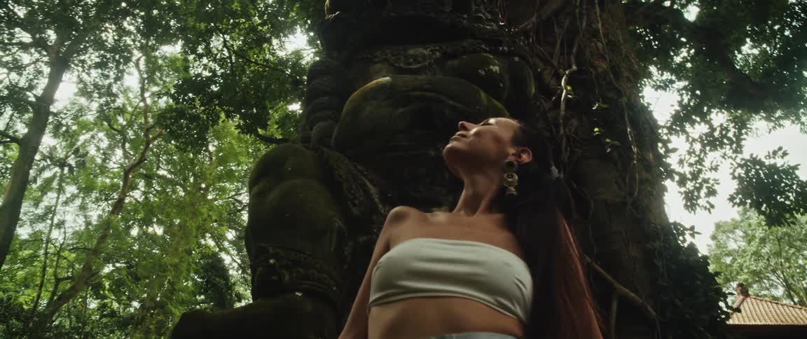 A spiritual woman finds tranquility as she stands beside a giant, moss-covered ancient statue deep within a lush jungle temple