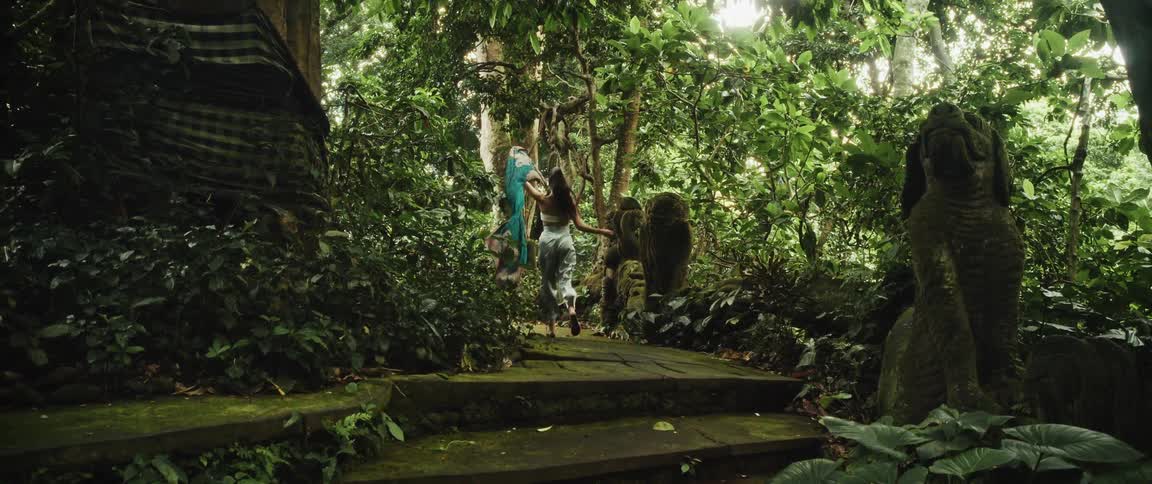 A woman with a flowing teal scarf gracefully ascends ancient stone stairs into a mysterious, lush jungle in slow motion