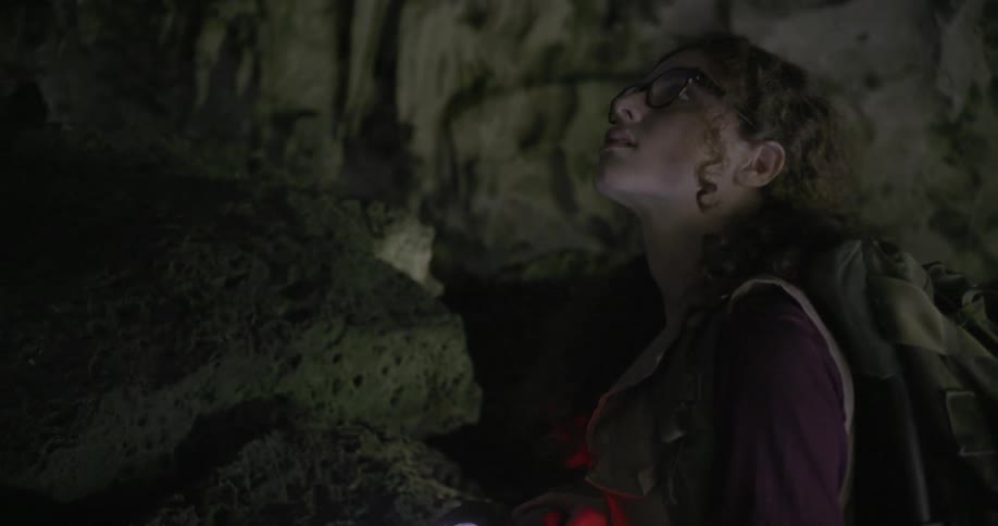 A woman searches a cave with a flashlight