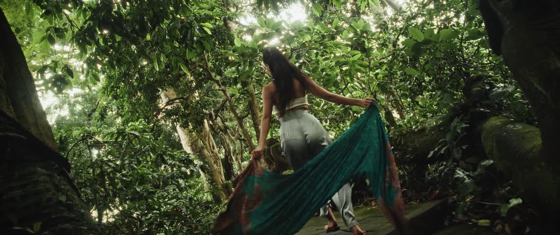 A mystical woman walks up ancient stone steps in a lush jungle, her flowing scarf billowing behind her in slow motion