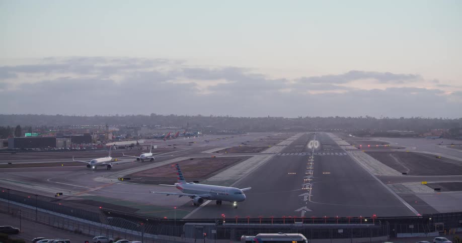 A passenger jet lands on a busy airport runway at dusk as other planes wait and taxi for takeoff