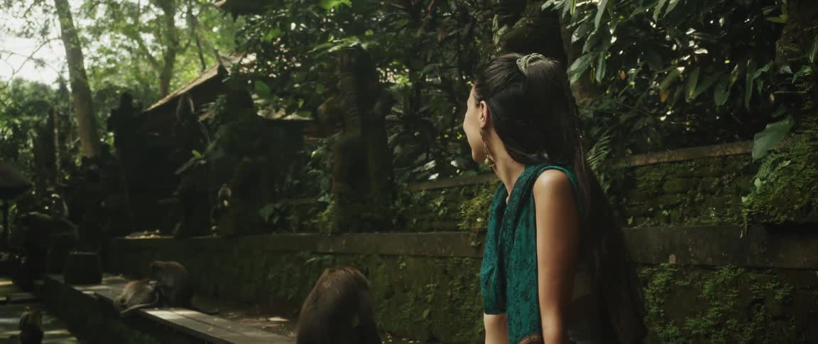 A young woman sits peacefully amongst monkeys in a lush, ancient jungle temple, smiling as she takes in the serene atmosphere