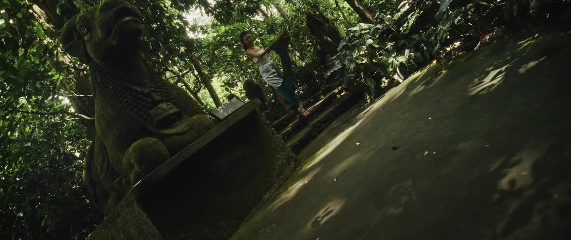 A woman gracefully dances with a flowing scarf down ancient stone steps in a lush, sun-dappled jungle temple
