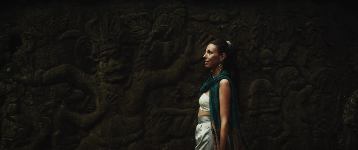 A woman explores an ancient temple in a lush jungle, marveling at the intricate, moss-covered stone carvings and statues