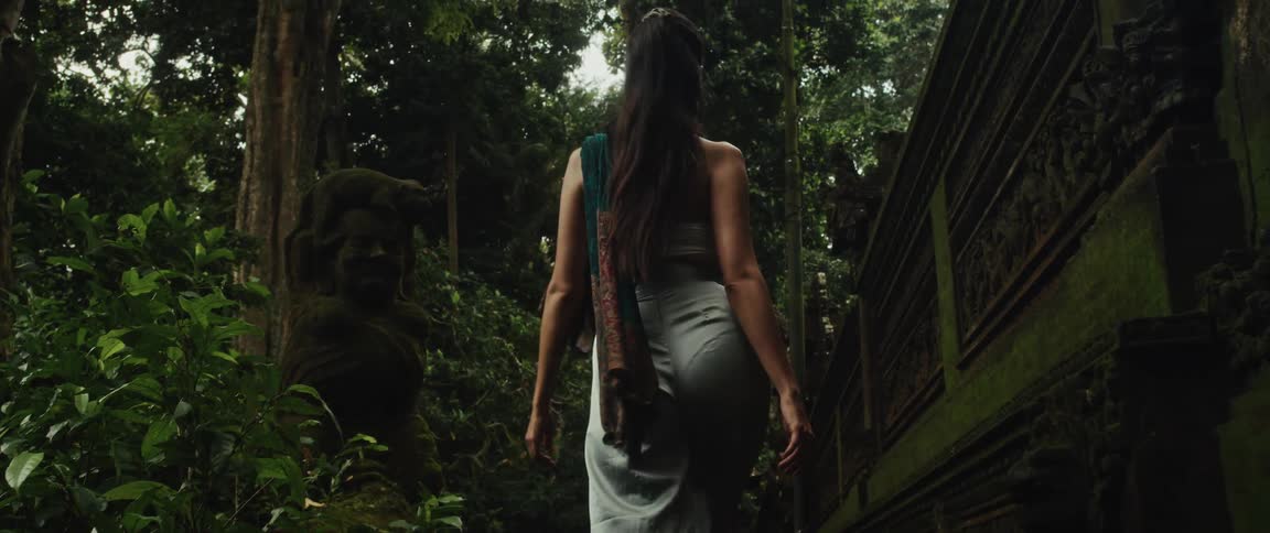 A woman slowly walks up ancient stone stairs and explores a mystical moss-covered temple deep within a lush jungle